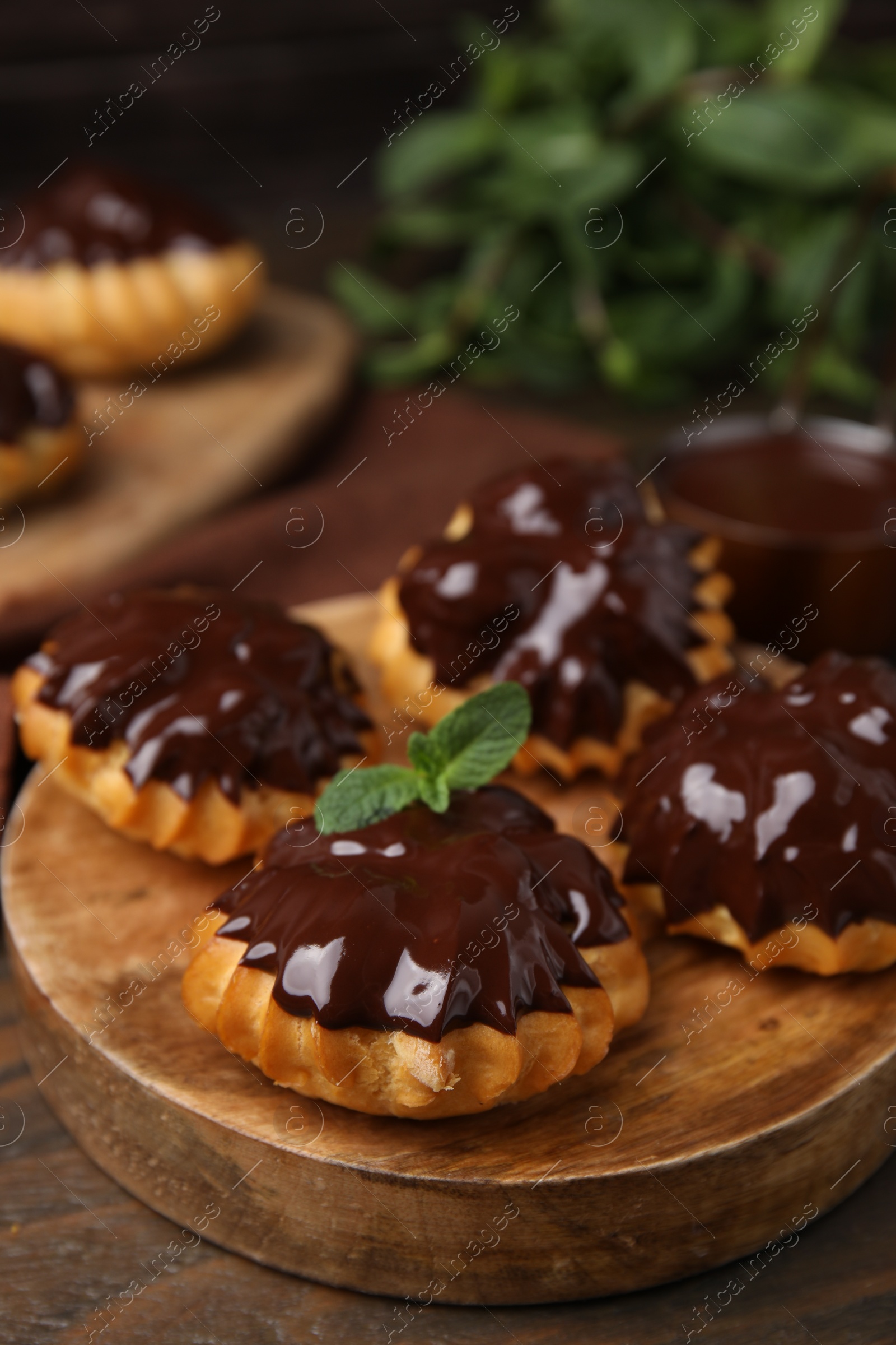 Photo of Delicious profiteroles with chocolate spread and mint on wooden table, closeup