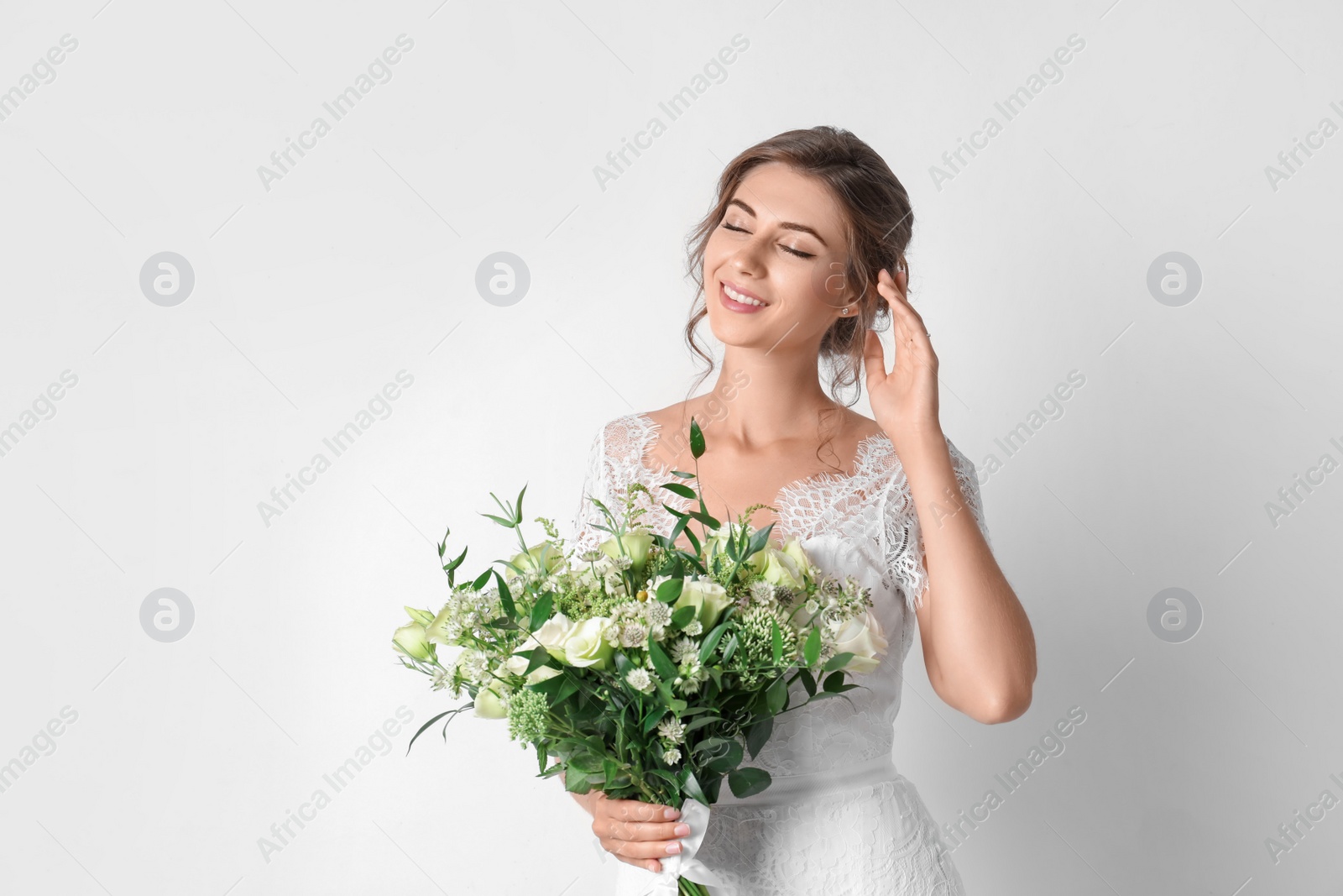 Photo of Young bride wearing wedding dress with beautiful bouquet on light background