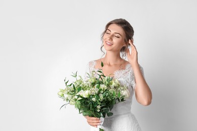 Young bride wearing wedding dress with beautiful bouquet on light background