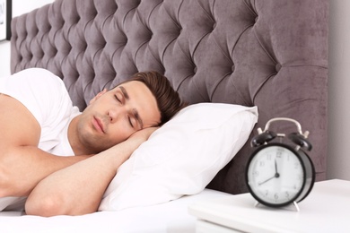 Photo of Young man sleeping in bed and alarm clock on nightstand at home