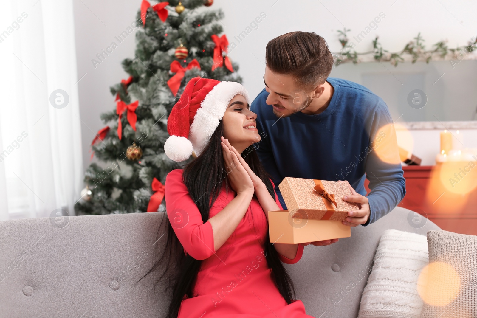 Photo of Young man giving gift box to girlfriend at home. Happy couple celebrating Christmas