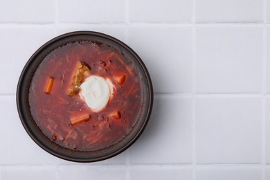 Photo of Tasty borscht with sour cream in bowl on white tiled table, top view. Space for text