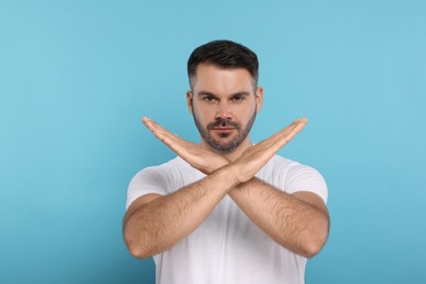 Photo of Handsome man with crossed hands on light blue background. Stop gesture