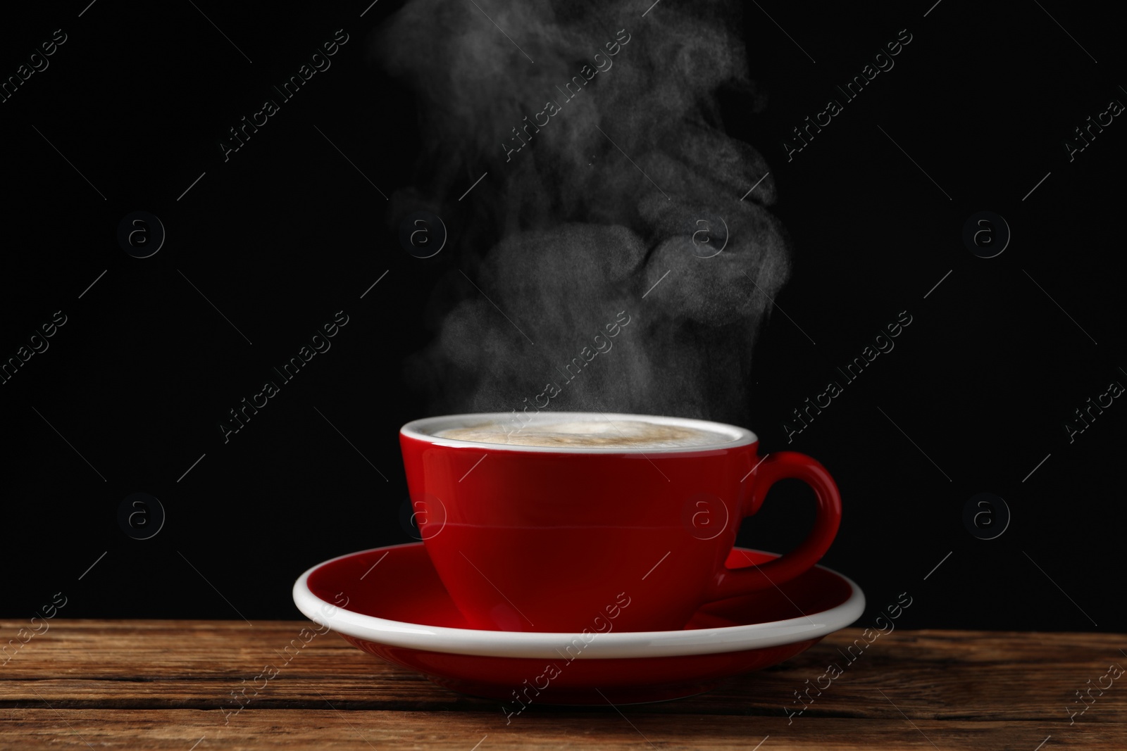 Image of Red cup with hot steaming coffee on wooden table against black background