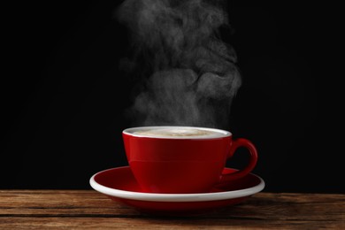 Image of Red cup with hot steaming coffee on wooden table against black background