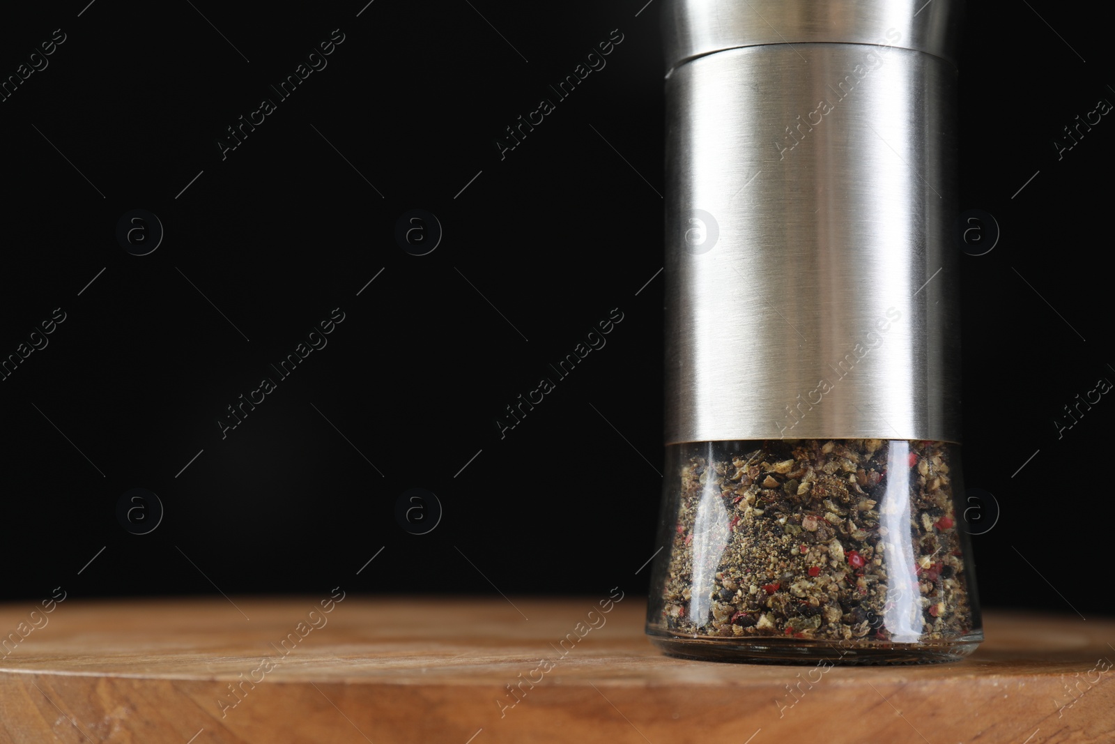 Photo of Pepper shaker on wooden board against black background, closeup. Space for text