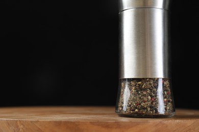 Photo of Pepper shaker on wooden board against black background, closeup. Space for text