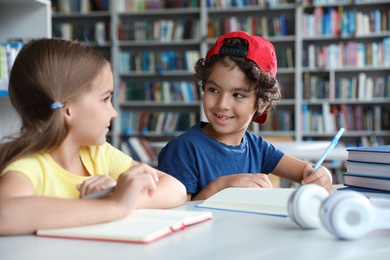 Photo of Little children writing at table with books in library reading room