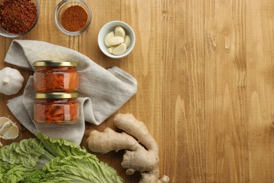 Photo of Delicious kimchi with Chinese cabbage and ingredients on wooden table, flat lay. Space for text