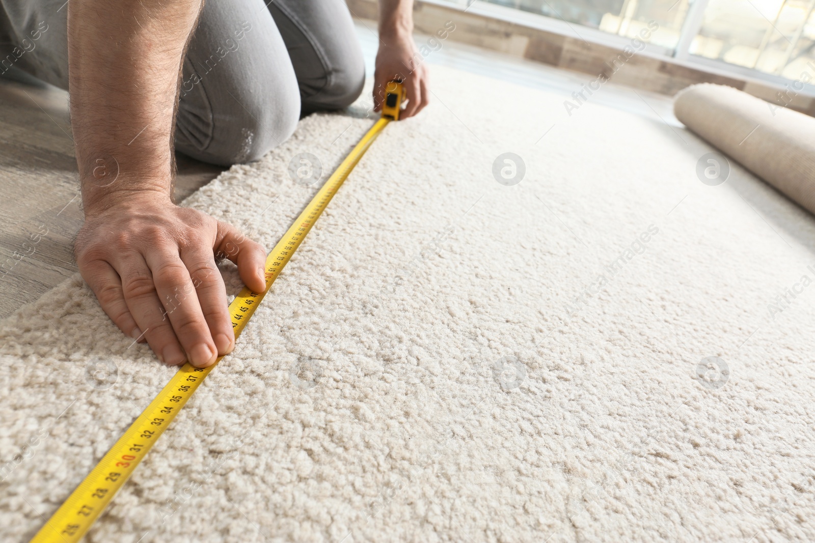 Photo of Man measuring carpet indoors, closeup view. Construction tool