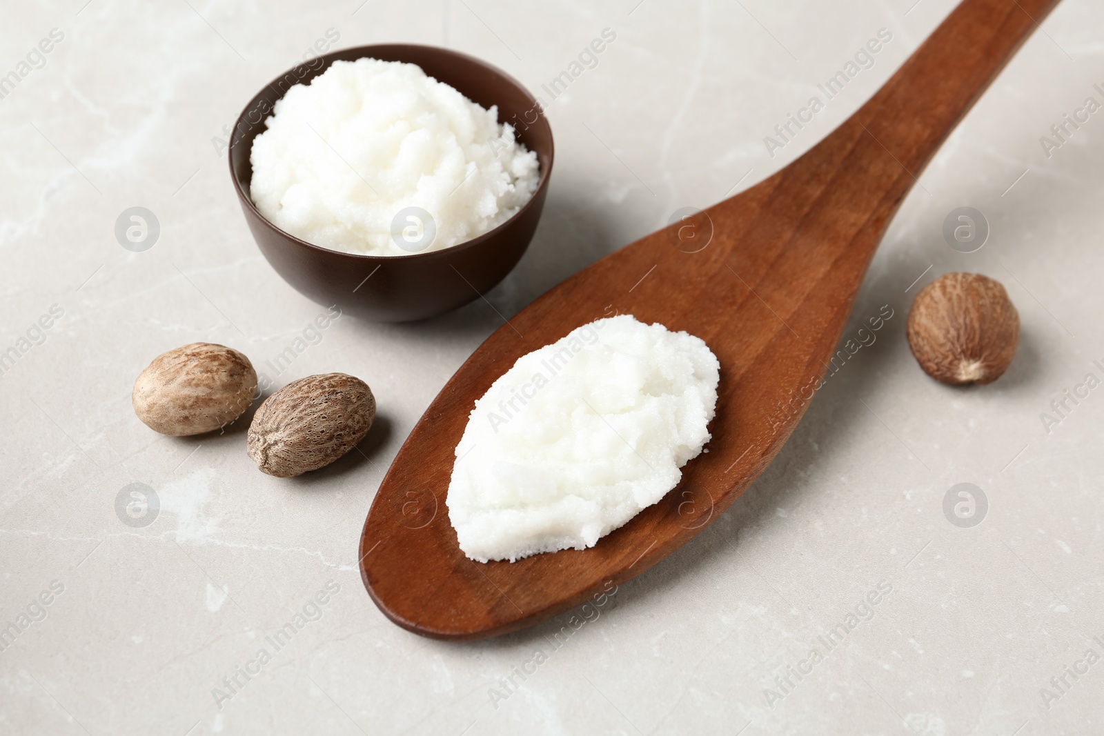 Photo of Shea butter in wooden spoon and bowl with nuts on table