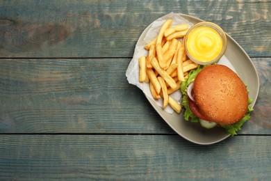 Photo of French fries, tasty burger and sauce on light blue wooden table, top view. Space for text