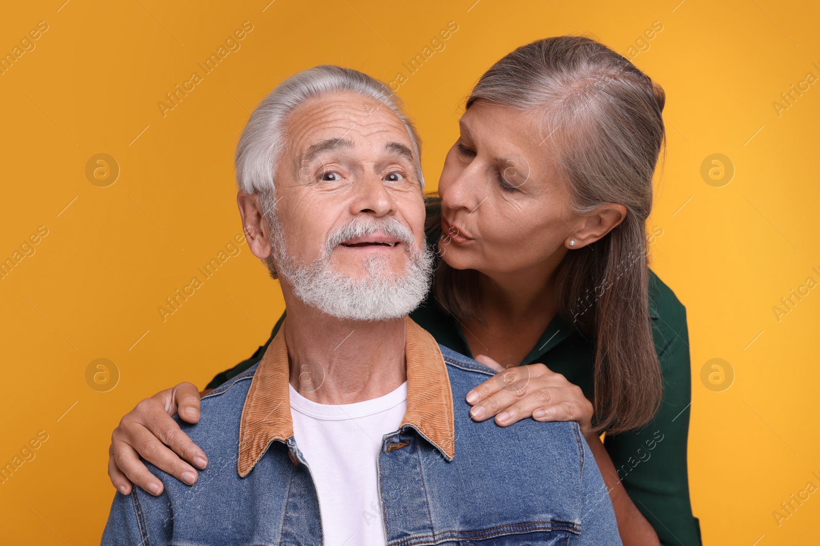 Photo of Senior woman kissing her beloved man on orange background