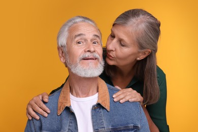 Senior woman kissing her beloved man on orange background