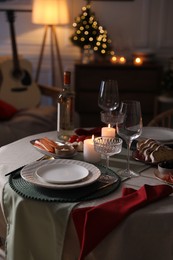 Photo of Christmas table setting with burning candles, appetizers and dishware indoors