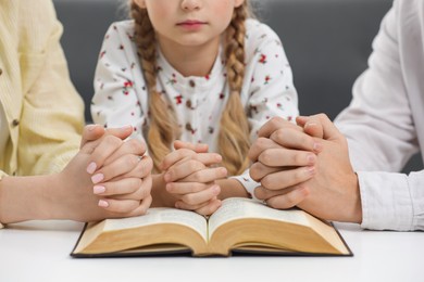 Girl and her godparents praying over Bible together at table indoors, closeup