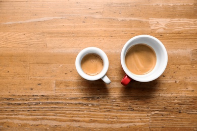 Cups of fresh coffee on wooden table, flat lay. Space for text