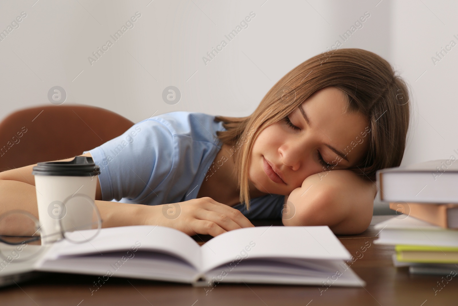 Photo of Young tired woman sleeping near books at wooden table indoors