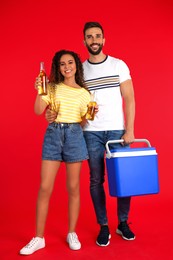 Photo of Happy couple with cool box and bottles of beer on red background