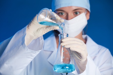 Photo of Female scientist pouring reagent into flask with sample on color background. Laboratory analysis