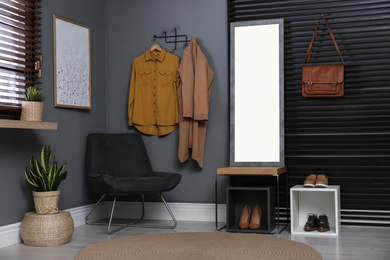 Hallway interior with modern furniture, mirror and hanging clothes