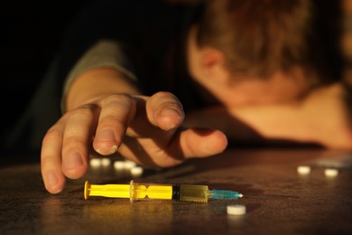 Photo of Addicted man reaching to drugs at grey textured table, focus on syringe