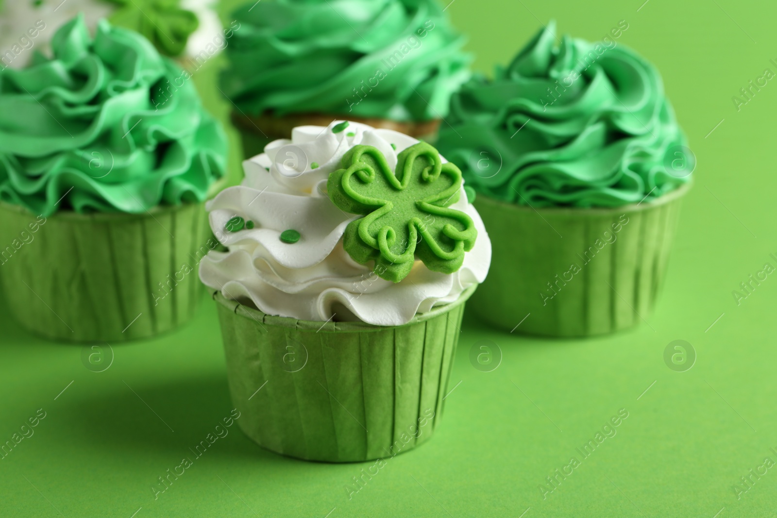 Photo of St. Patrick's day party. Tasty festively decorated cupcakes on green background, closeup