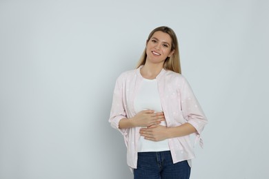 Photo of Happy woman touching her belly on light background, space for text. Concept of healthy stomach