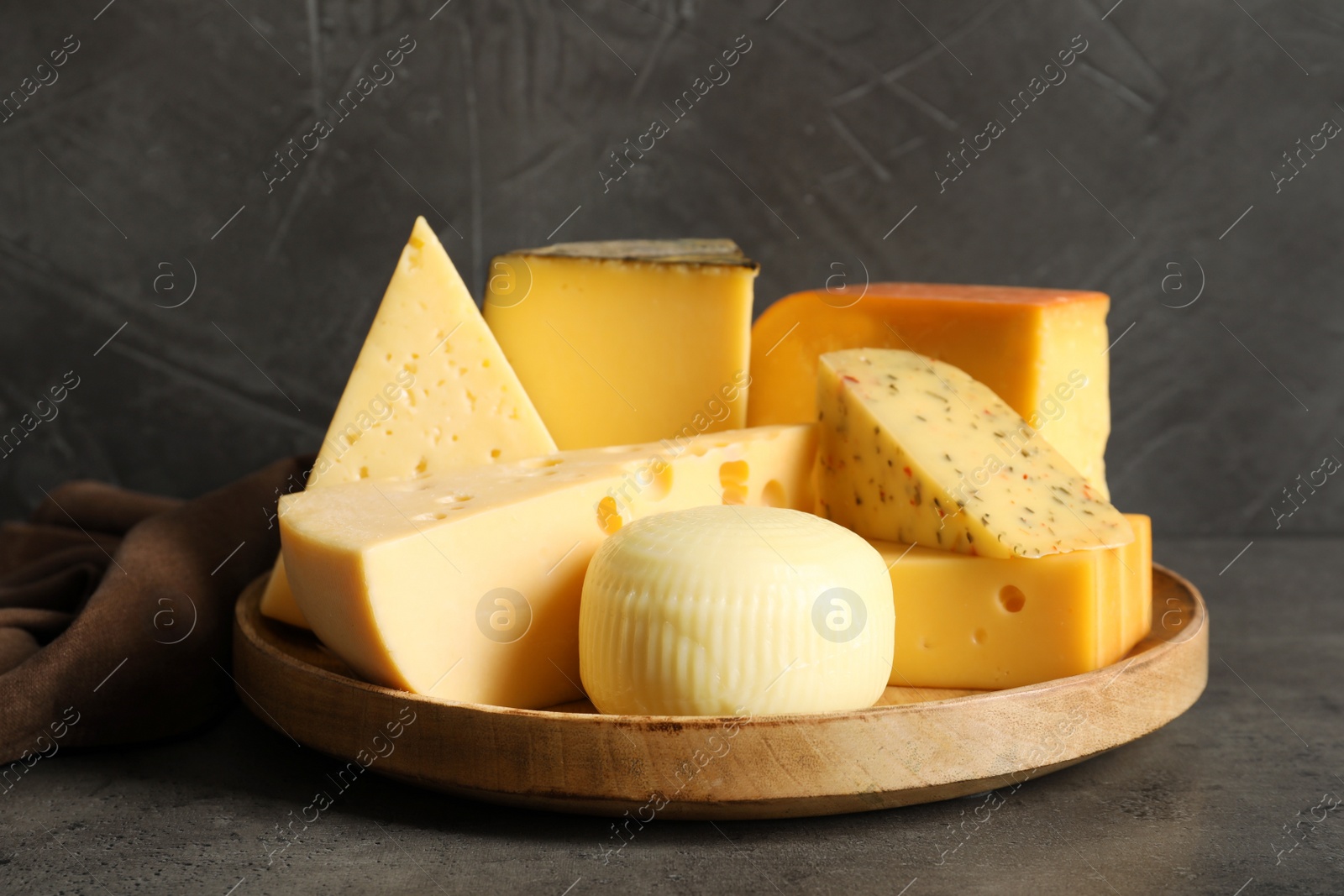 Photo of Wooden plate with different sorts of cheese on grey table