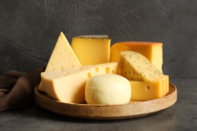 Photo of Wooden plate with different sorts of cheese on grey table