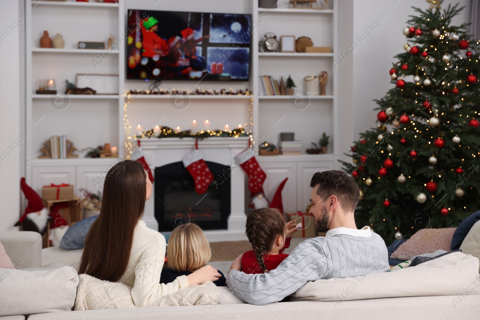 Photo of Happy family spending time on sofa near TV in cosy room, back view. Christmas atmosphere