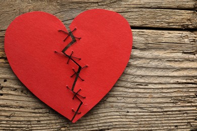 Photo of Broken heart. Torn red paper heart sewed with thread on wooden table, top view. Space for text