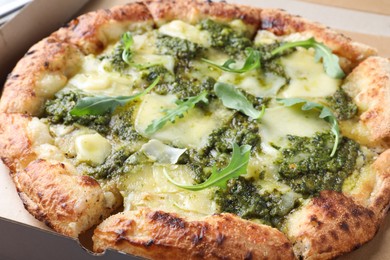 Photo of Delicious pizza with pesto, cheese and arugula in cardboard box, closeup