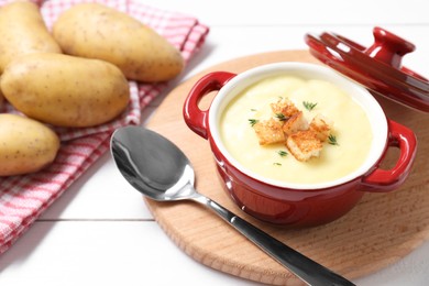 Photo of Tasty potato soup with croutons in ceramic pot and spoon on white wooden table