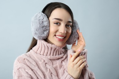 Photo of Beautiful young woman wearing earmuffs on light grey background