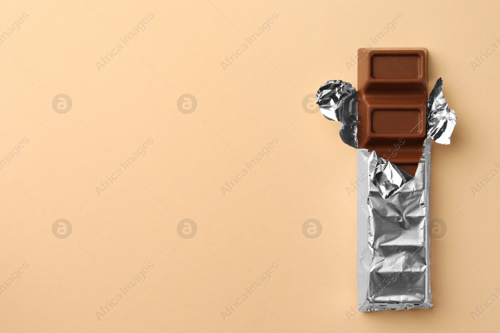 Photo of Delicious chocolate bar wrapped in foil on beige background, top view. Space for text