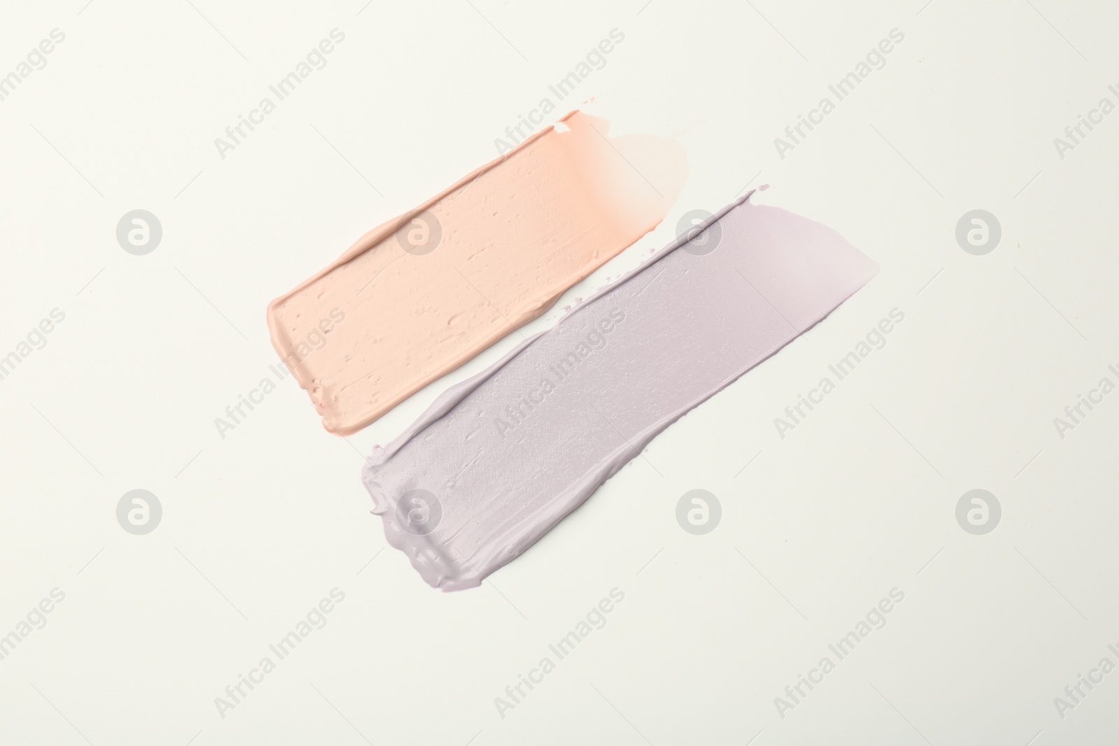 Photo of Strokes of pink and purple color correcting concealers on white background