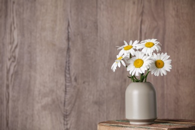 Beautiful tender chamomile flowers in vase on table against wooden background, space for text