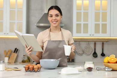 Young woman with recipe book cooking in kitchen