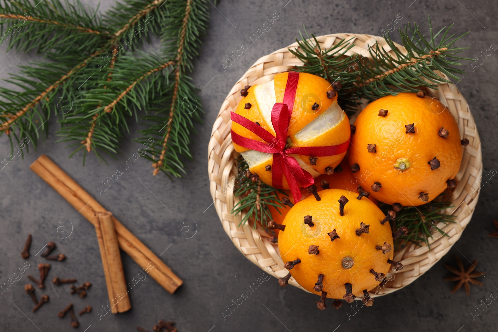 Photo of Pomander balls made of tangerines with cloves, spices and fir branches on grey table, flat lay