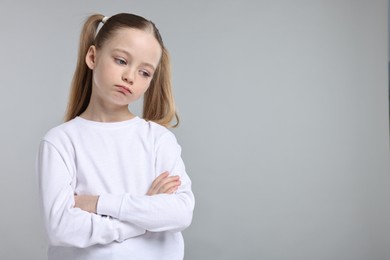 Portrait of sad girl with crossed arms on light grey background, space for text