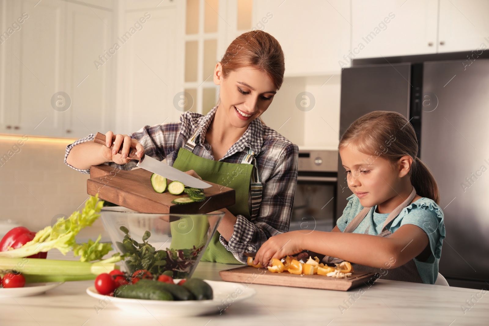 Photo of Mother and daughter cooking salad together in kitchen