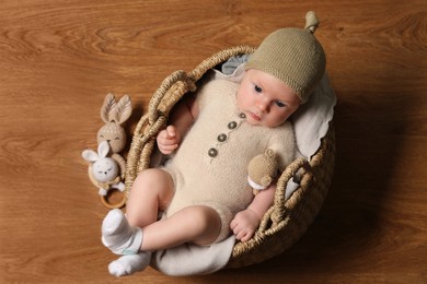 Photo of Cute little baby with knitted bear toy in wicker basket, top view