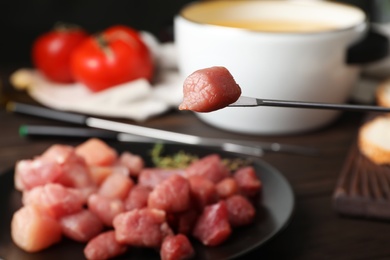 Raw meat fondue piece on fork over table, closeup. Space for text