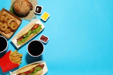 Photo of Tasty burger, hot dogs, fried onion rings, different sauces and refreshing drinks on light blue background, flat lay with space for text. Fast food