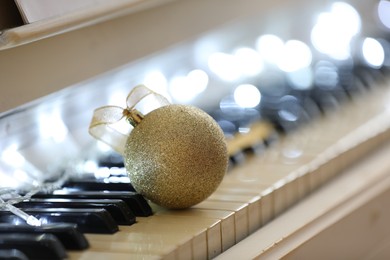 Photo of Beautiful golden bauble and fairy lights on piano keys, closeup. Christmas music