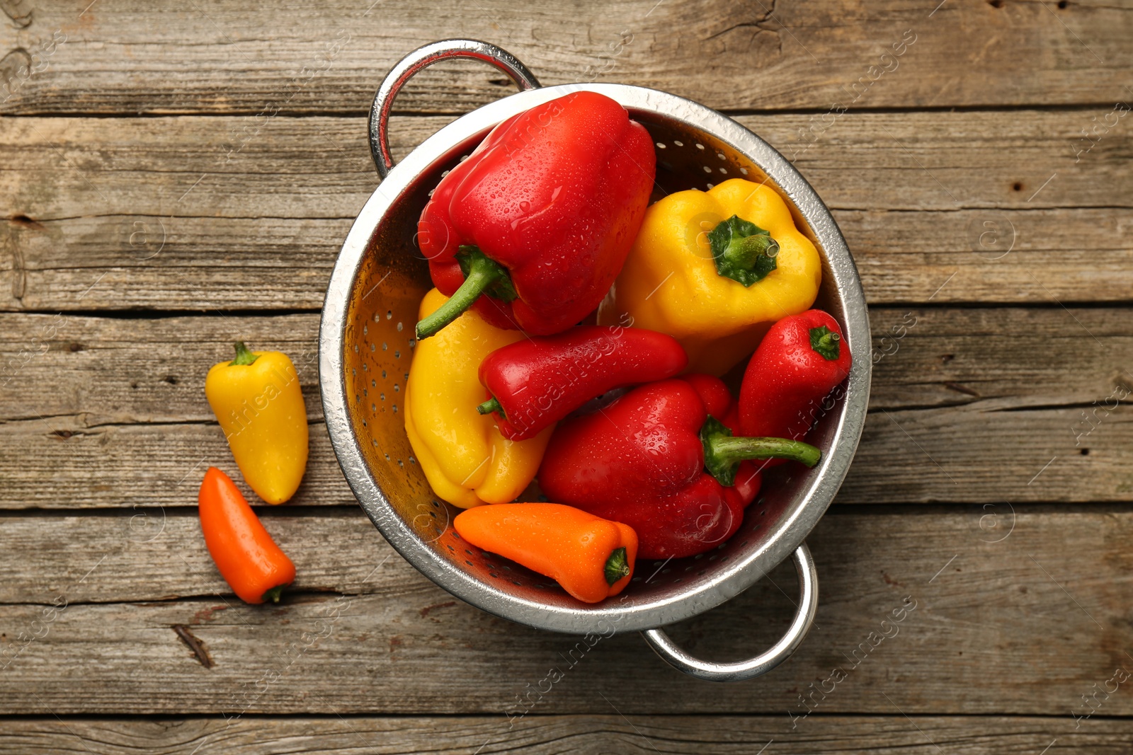 Photo of Metal colander with fresh peppers on wooden table, top view