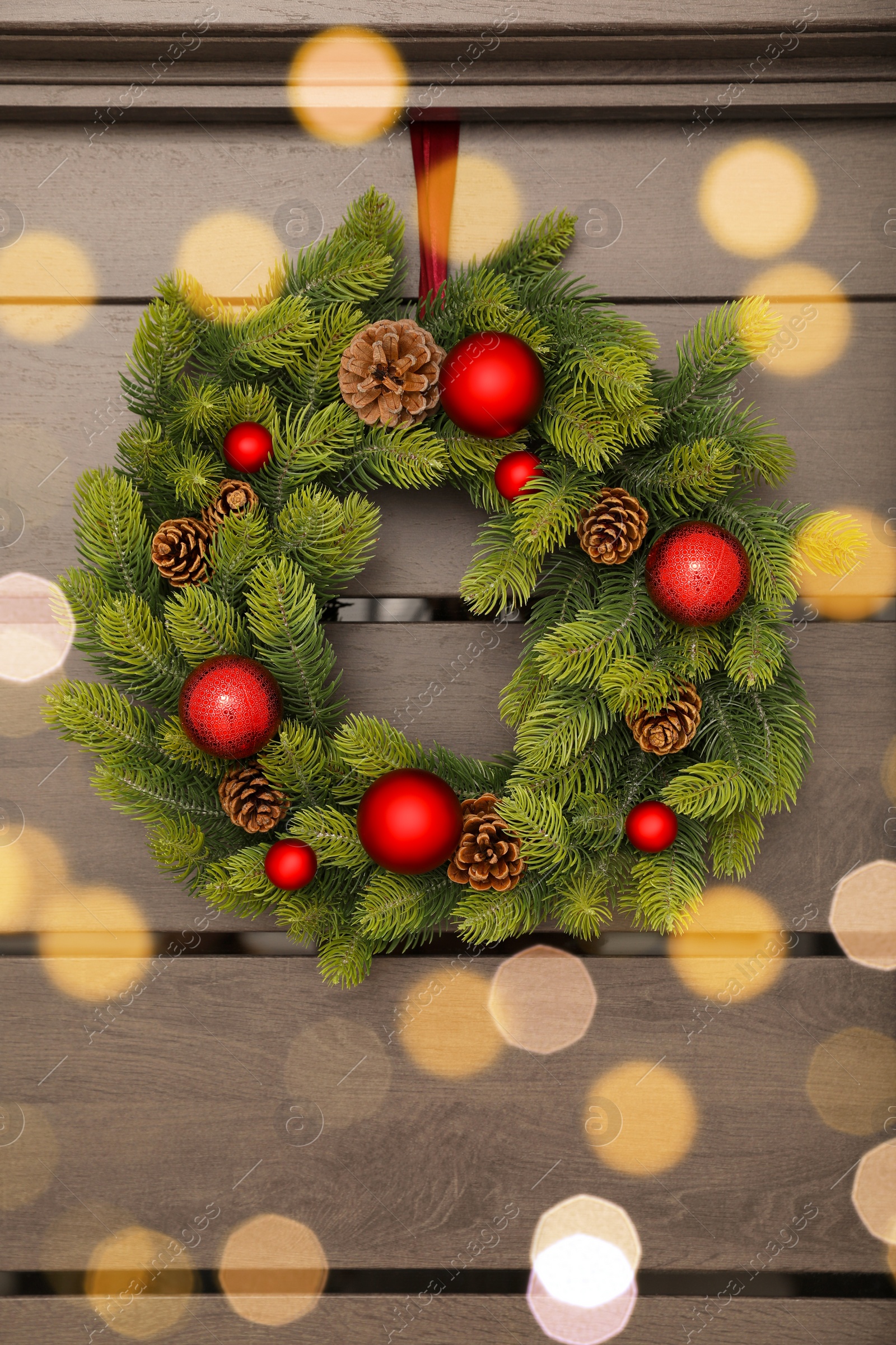 Photo of Christmas wreath with red baubles and cones hanging on wooden door