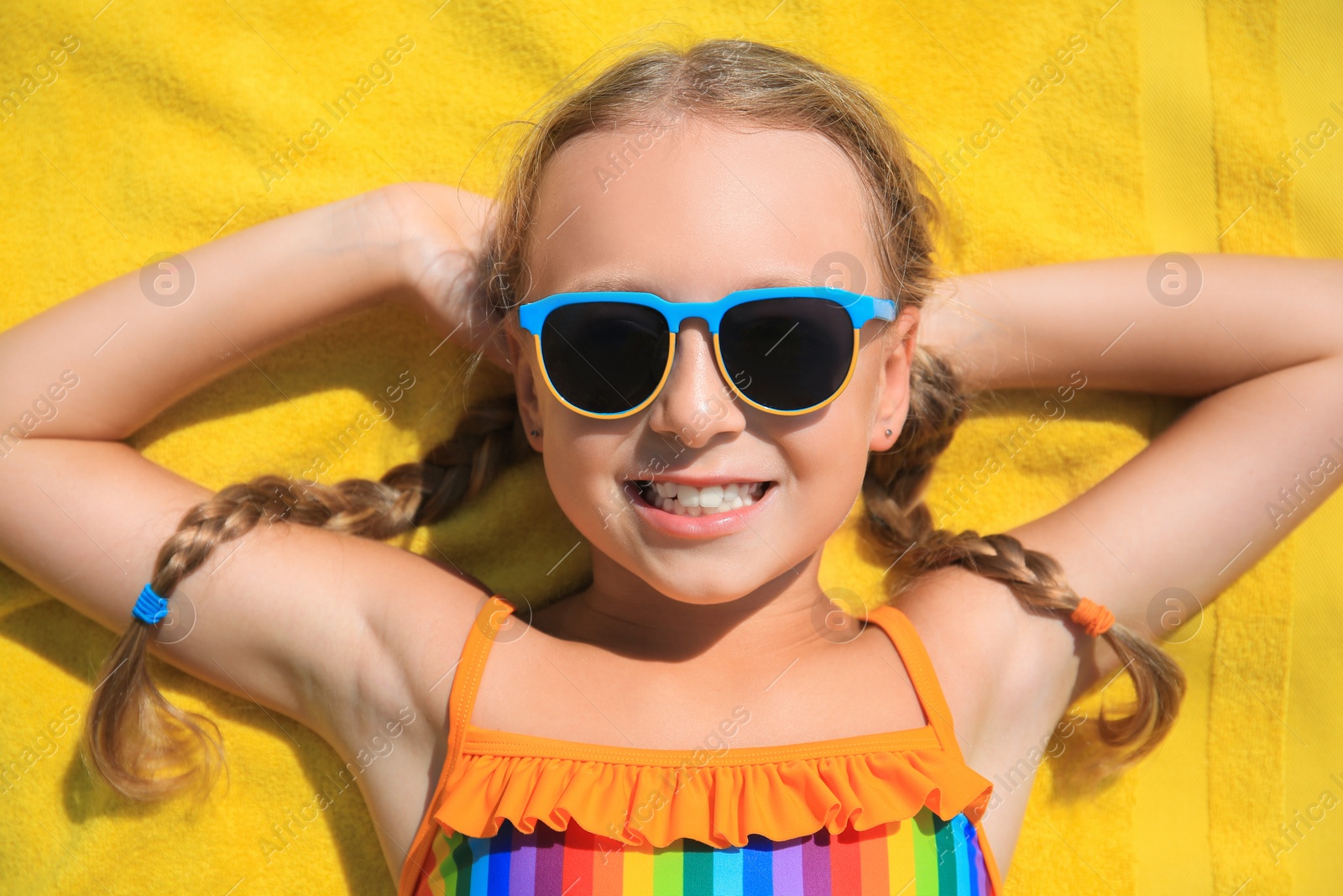 Photo of Happy little girl in sunglasses lying on beach towel outdoors, top view