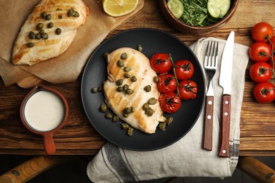 Delicious cooked chicken fillet with capers and tomatoes served on wooden table, flat lay